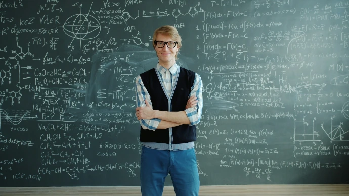 Man in glasses stands before a chalkboard with equations.